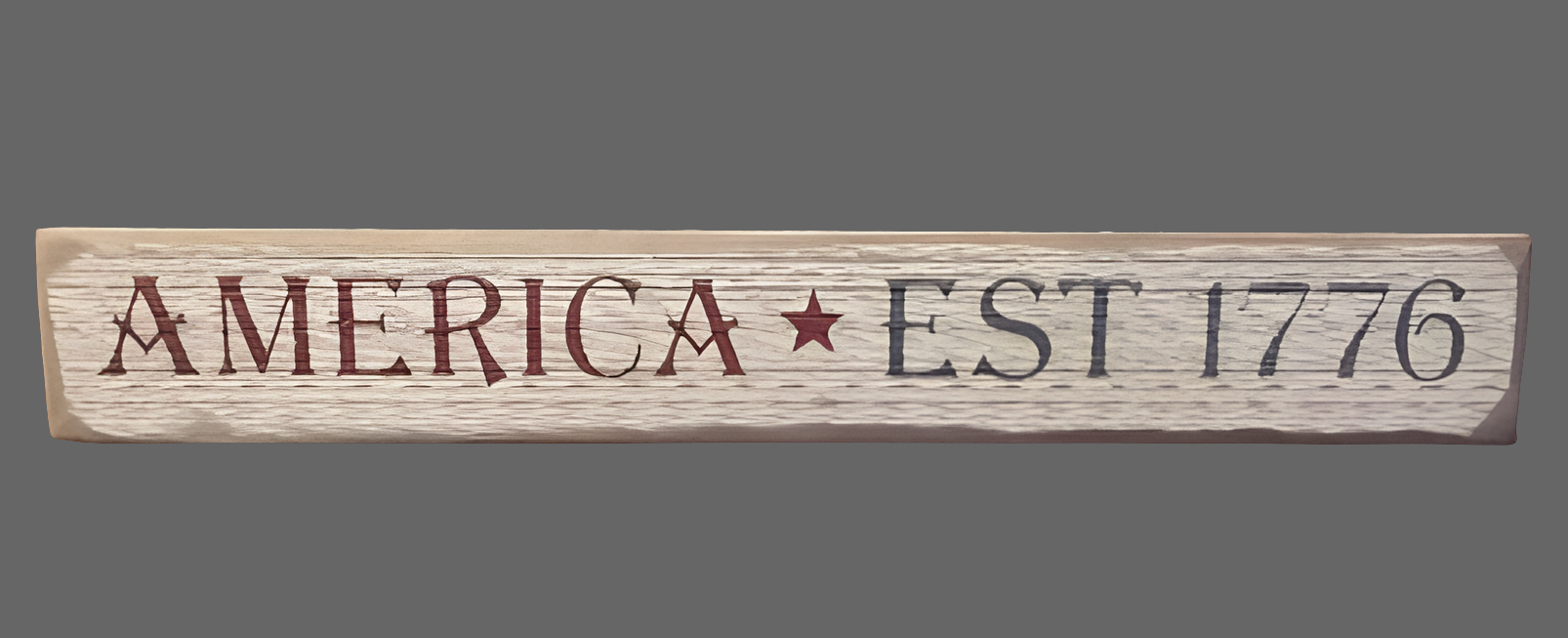 A wooden sign with the text 'AMERICA EST. 1776' in white and red, with a star symbol, on a wooden surface.