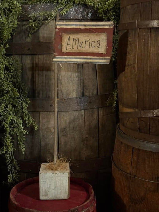 Decorative sign with 'America' on a wooden stand against a rustic wooden wall.