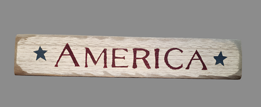 A wooden sign with the word 'America' printed in bold red letters, surrounded by star graphics, on a wooden surface.