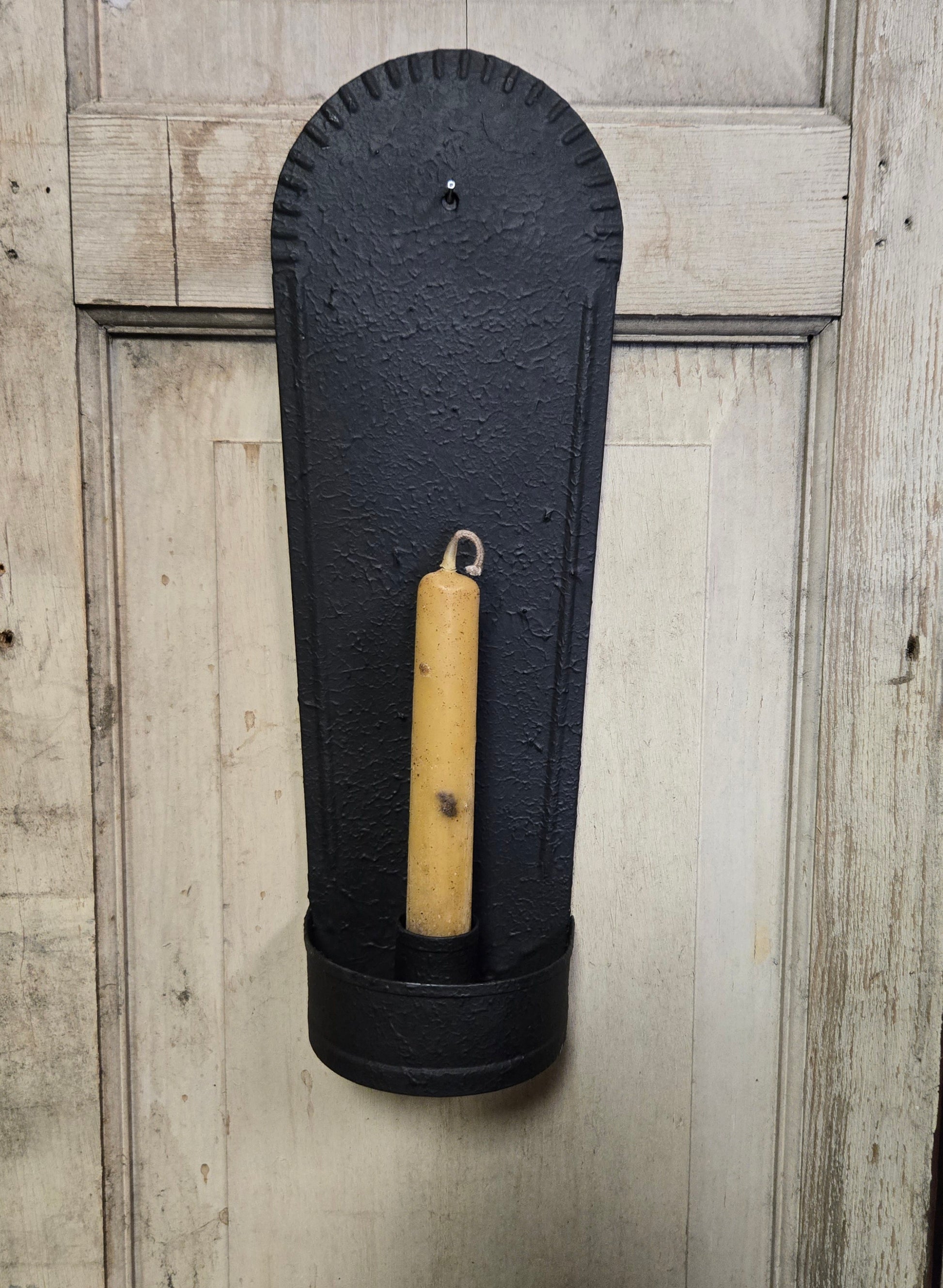 Black wall-mounted candle holder with a beige candle against a wooden background
