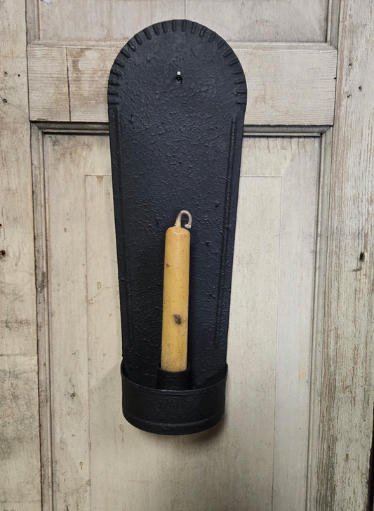 Black wall-mounted candle holder with a beige candle against a wooden background