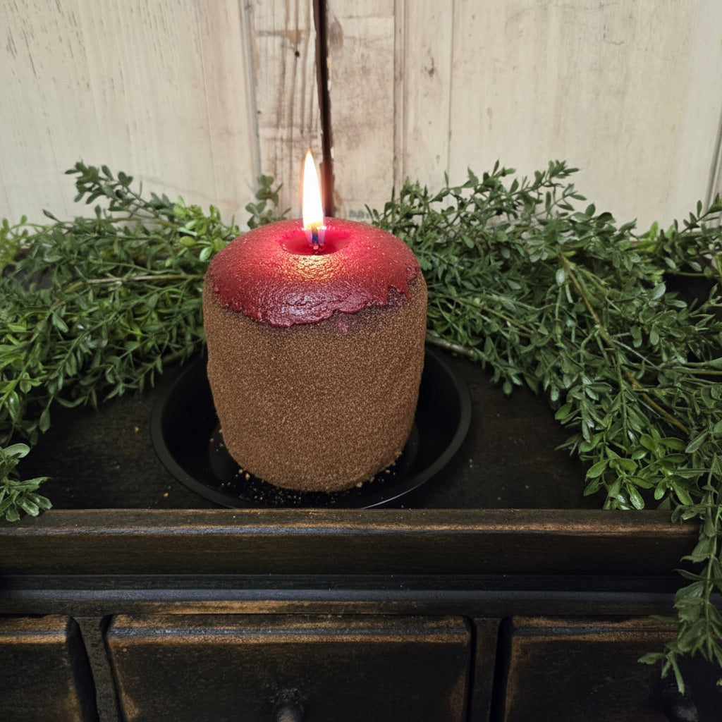 Coated candle sitting on candle pan and tray with greenery