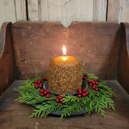Gold glittery candle with greenery and red berries on a wooden surface