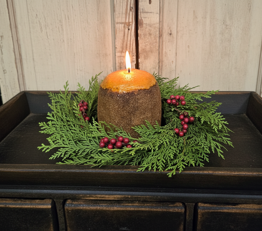 Decorative candle with greenery and berries on a wooden surface