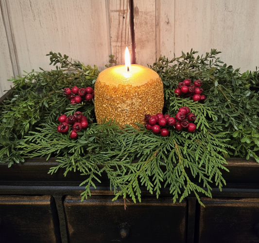 Decorative arrangement with a lit candle, greenery, and red berries on a wooden surface.