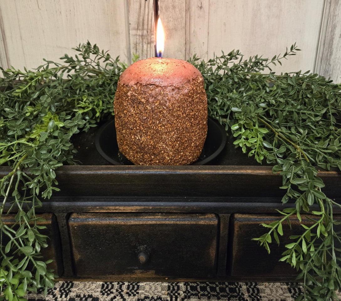 Coated candle sitting on a wood tray with greenery