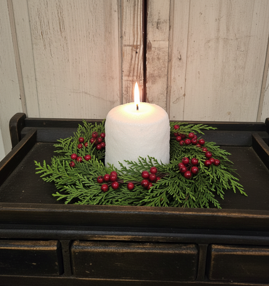 White candle on a wooden tray with greenery and red berries against a wooden background