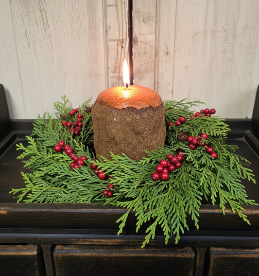 Candle with greenery and berries on a wooden surface