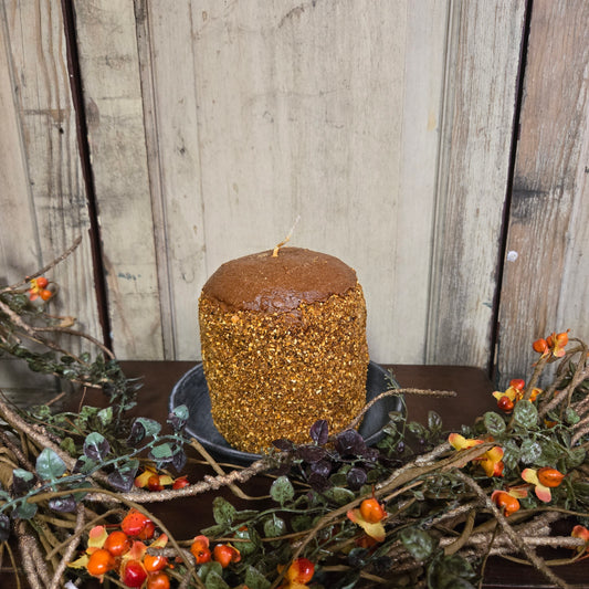 Decorative wreath with berries and a textured brown candle against a wooden background