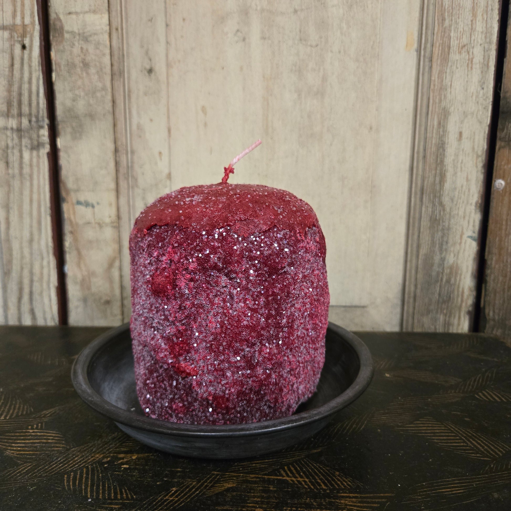 Red candle with glitter in a tin container on a wooden surface