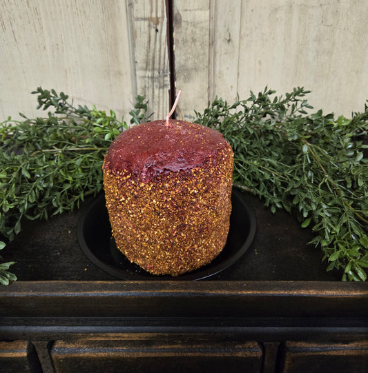 A spicy cranberry scented hearth candle placed on a black holder, with a rustic wooden background and greenery around it.