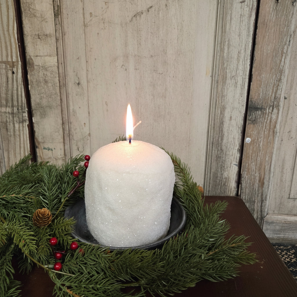 Decorative white glittered candle with greenery and berries on a wooden surface