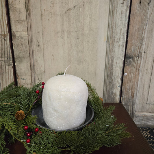 Decorative white glittered candle with greenery and berries on a wooden surface