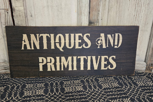 Wood sign hand painted with the words 'ANTIQUES AND PRIMITIVES'