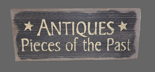A wooden sign with the text 'ANTIQUES PIECES OF THE PAST' distressed in a rustic style.