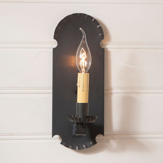 Black wall sconce with a lit bulb on a white wall