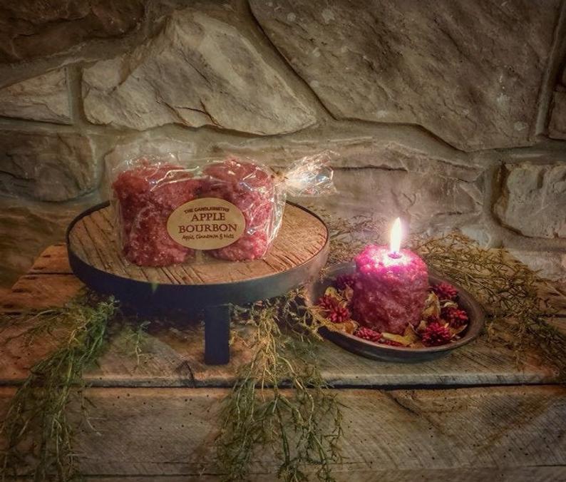 Red burning candle next to greenery and a riser with two candles in packaging