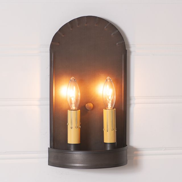 Wall-mounted light fixture with two illuminated bulbs on a white wall.