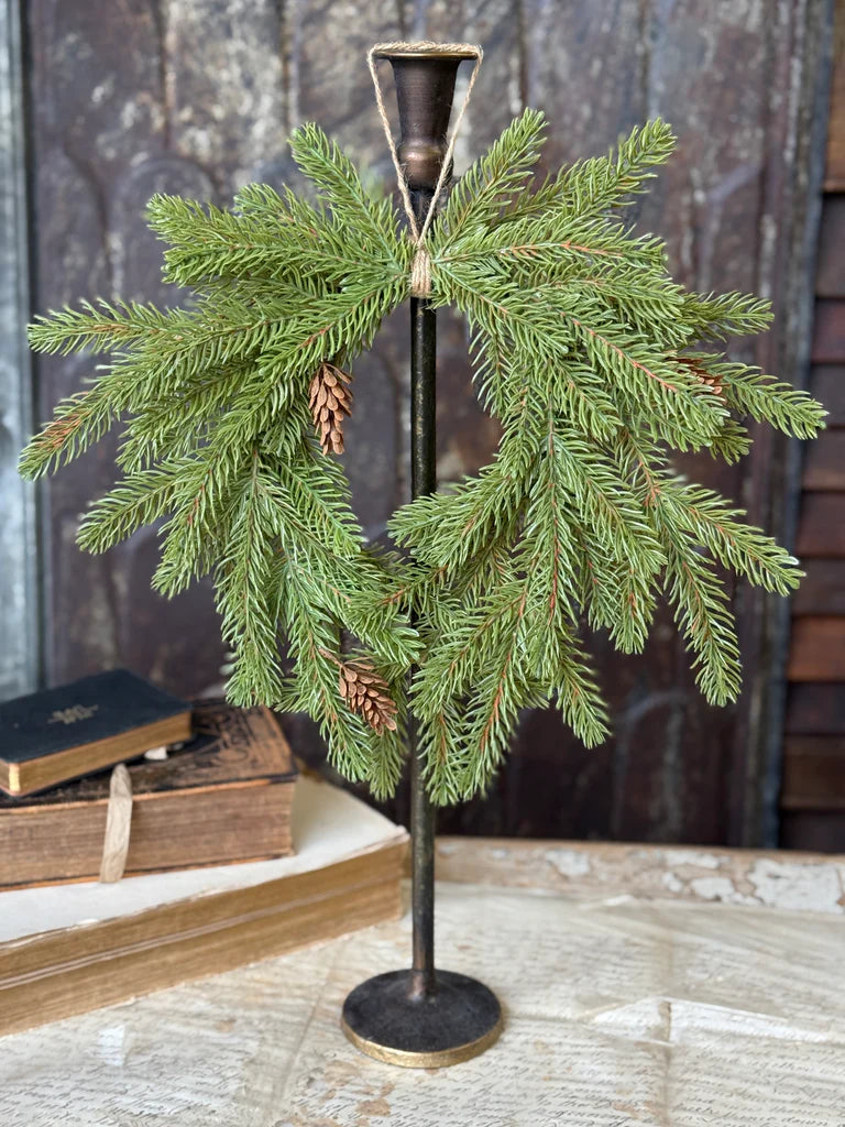 Decorative stand with green branches and pine cones on a wooden surface.