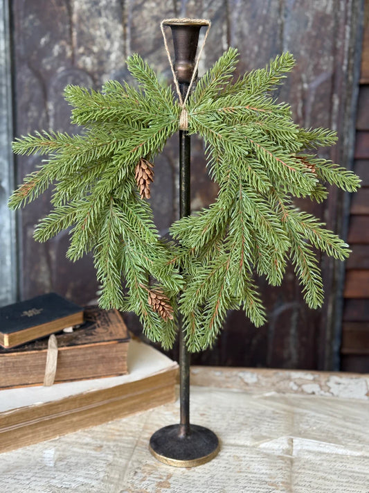 Decorative stand with green branches and pine cones on a wooden surface.