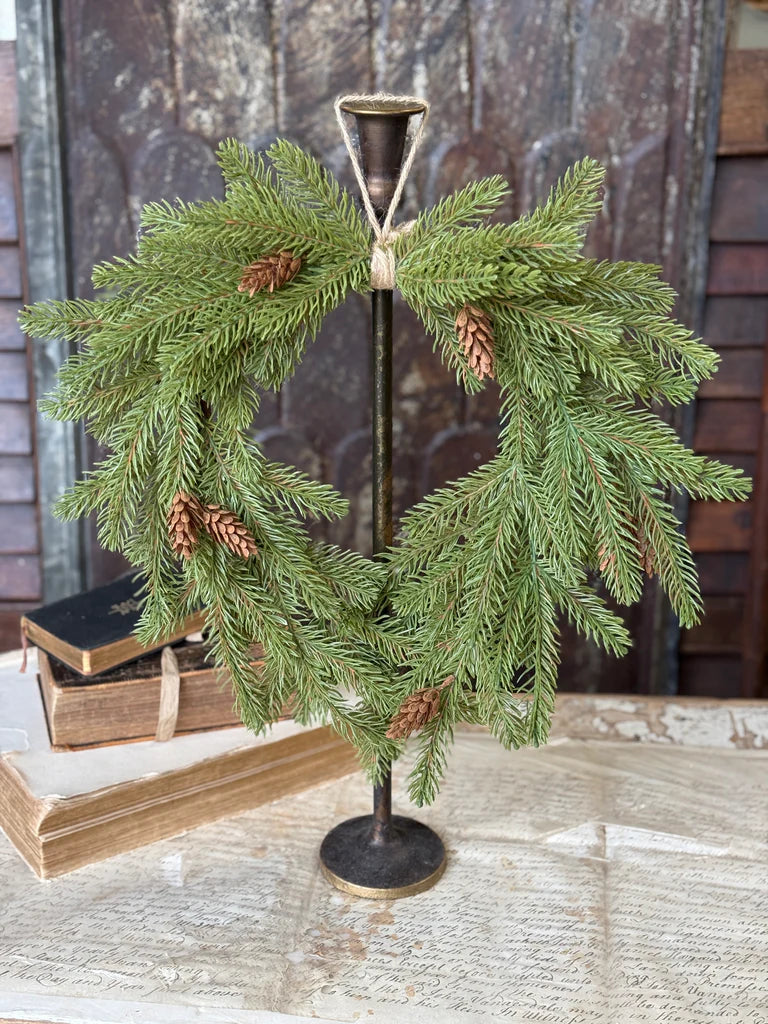 Decorative wreath with pine branches and cones on a stand against a rustic background