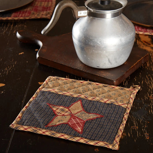Quilted placemat with star design on a wooden surface with a teapot and flowers.
