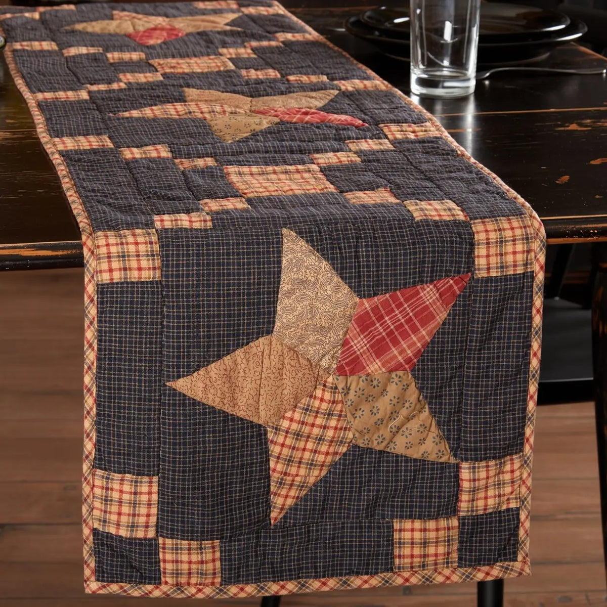 Arlington Star quilted table runner draped over a dark wood table, with tan and red patchwork stars on a dark plaid background.