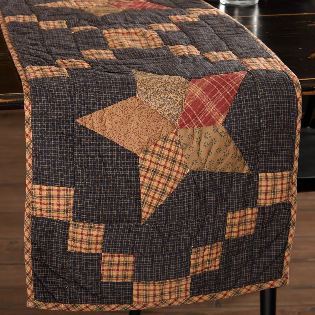 A rustic patchwork quilt table runner draped over a dark wooden table, featuring a large star motif in plaid and floral fabrics.