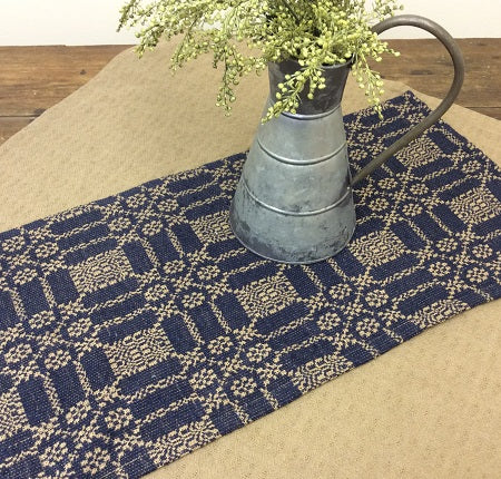 Navy blue and beige patterned table runner with a metal pitcher and greenery on a wooden surface.