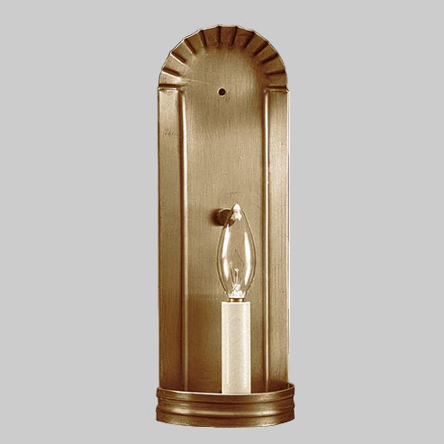 Brass wall sconce with a clear light bulb on a gray background