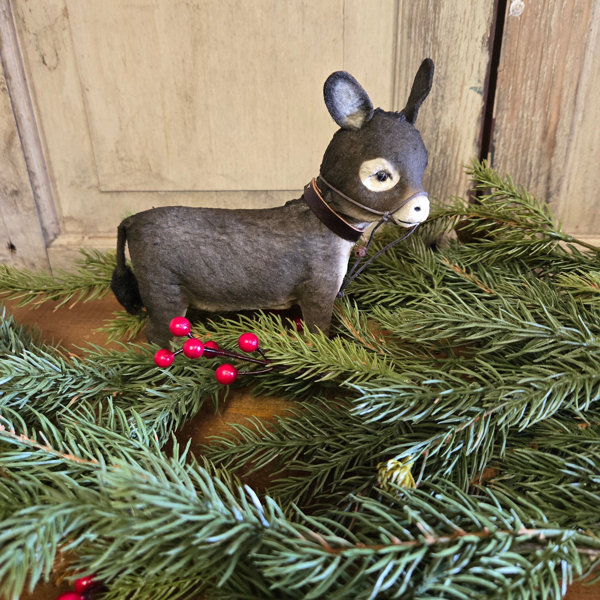 A paper mache figurine of a baby donkey with a collar, standing amongst pine branch decorations.