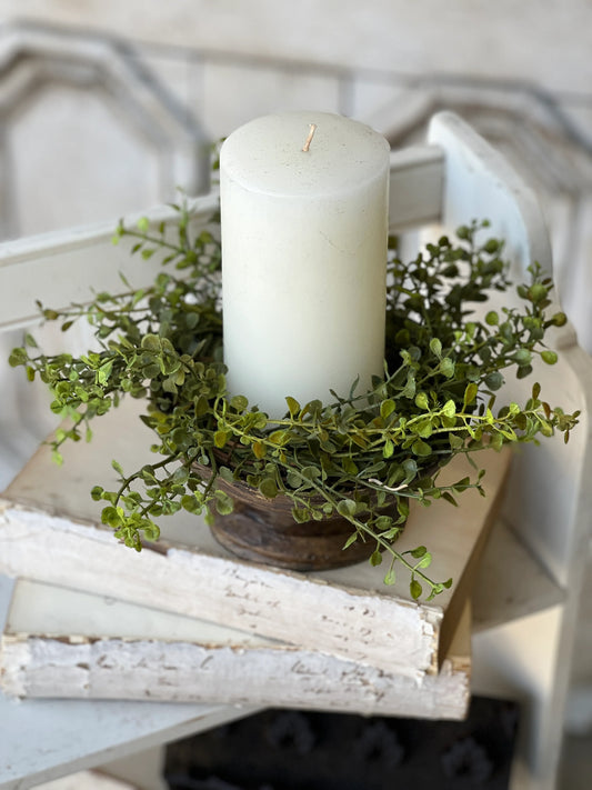 A candle ring decorated with artificial greenery placed on top of a white surface.