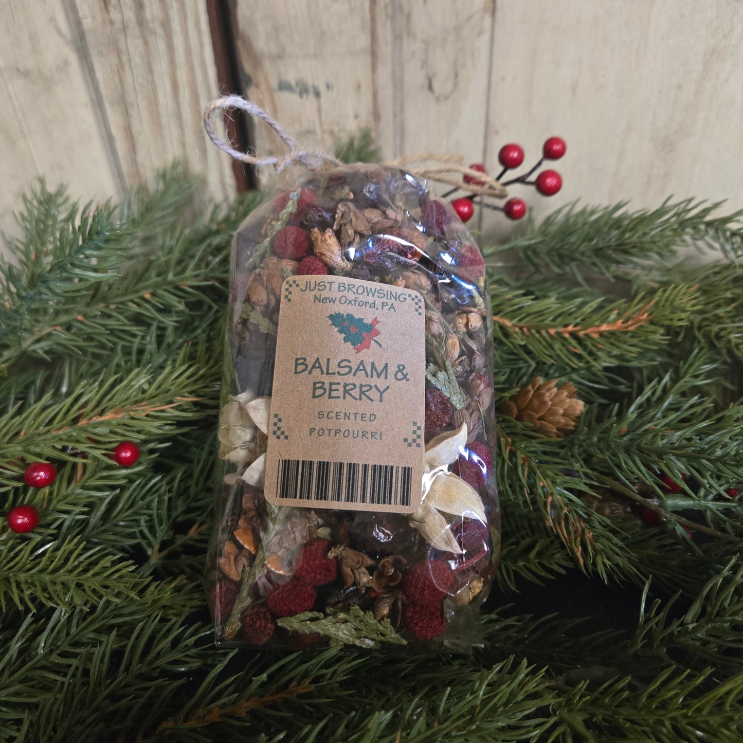 Packaged balsam and berry potpourri on a wooden surface with greenery.