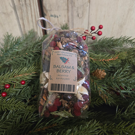 Packaged balsam and berry potpourri on a wooden surface with greenery.