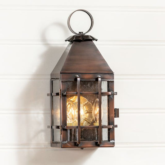 An outdoor wall light fixture with a solid antique copper finish, featuring a lantern design with visible wiring and a lit candle-like bulb within.