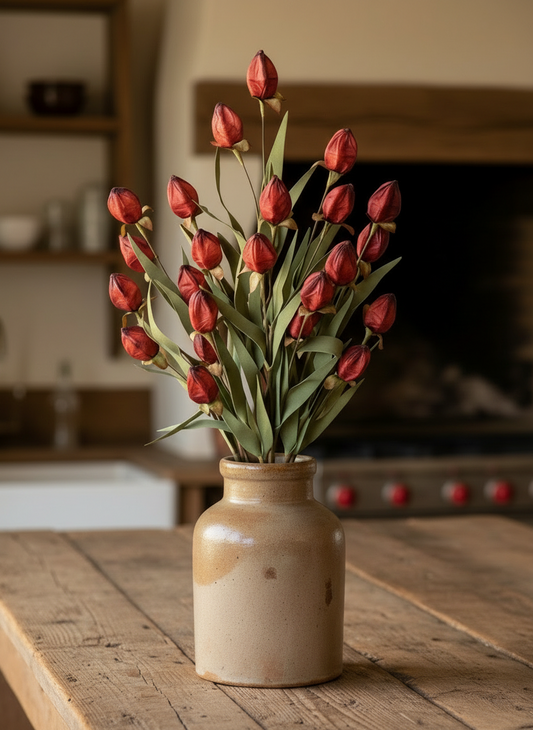 Bouquet of red tulips in a ceramic vase on a wooden table with a blurred kitchen background.