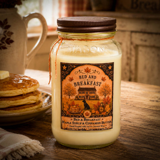 Jar of 'Bed and Breakfast' candle with a label on a wooden table with pancakes and a teapot.