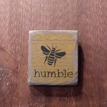 A rectangular wooden sign with a yellow background, featuring a black bee illustration and the word 'Humble' on it.