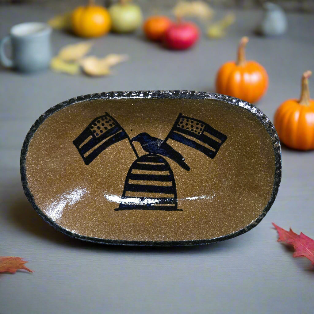 Decorative stoneware plate with bee skep and flag design on a table with pumpkins and leaves.