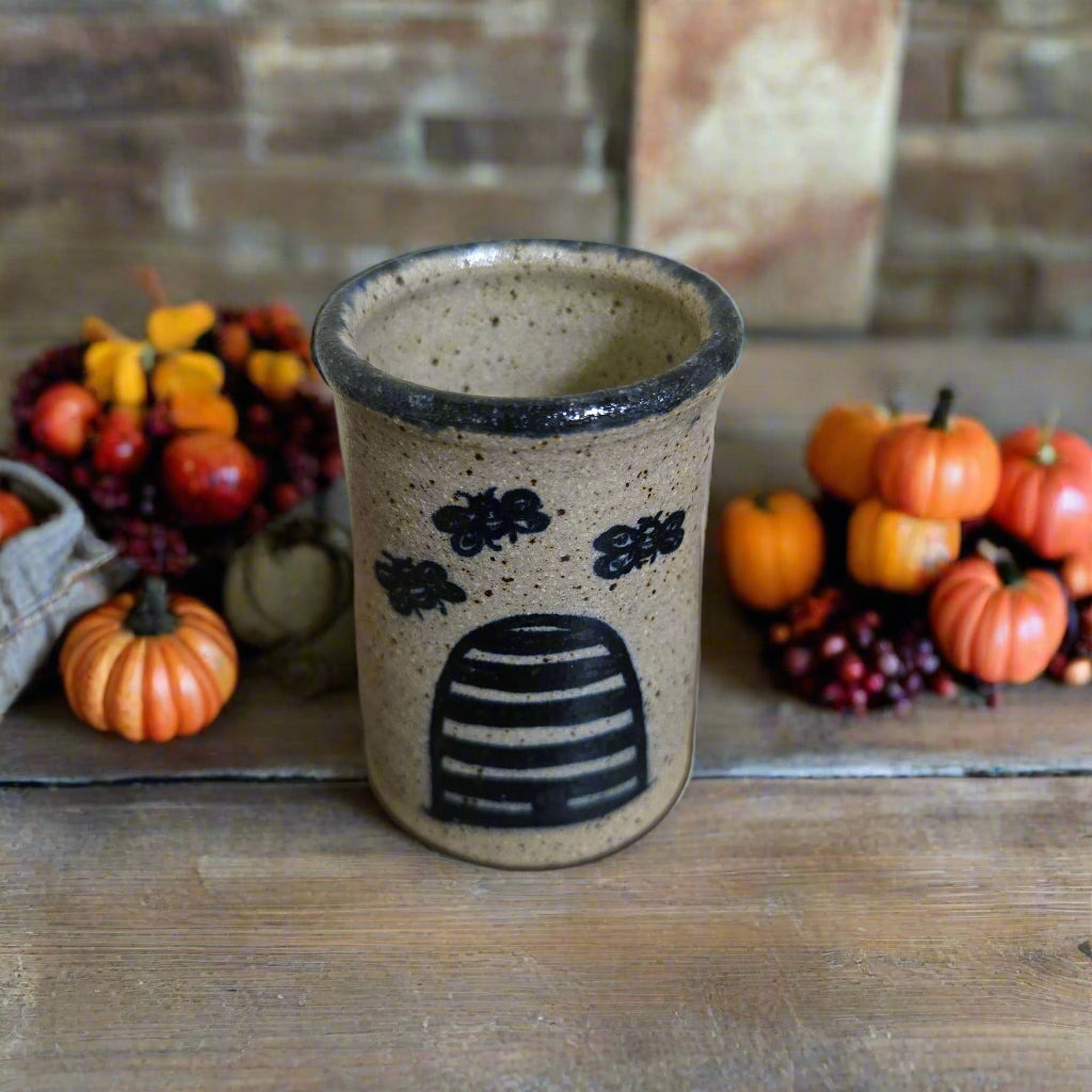 Ceramic cup with bee hive design on a wooden surface with pumpkins and berries in the background.