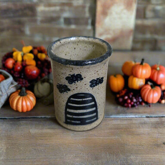 Ceramic cup with bee hive design on a wooden surface with pumpkins and berries in the background.