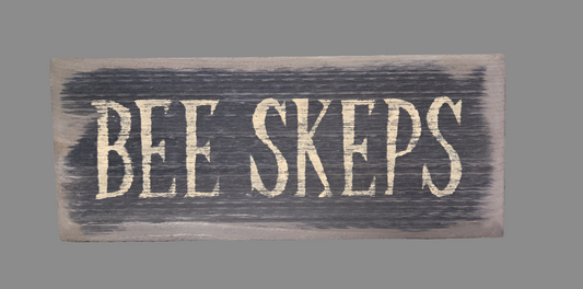 A wooden sign with the words 'BEE SKEPS' written in black.
