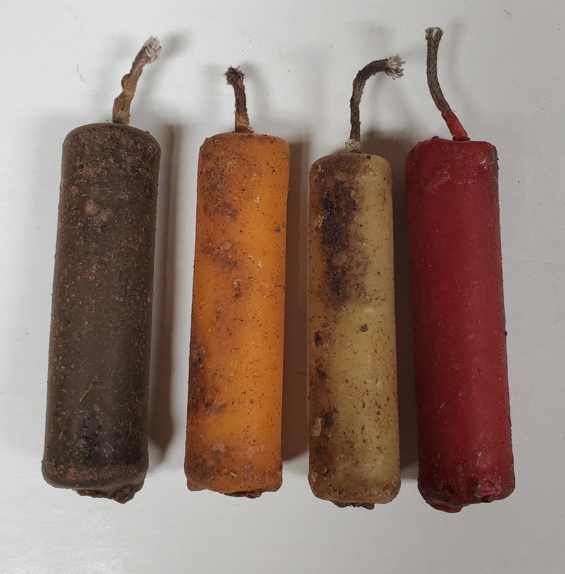 A set of four beeswax tapers in different colors including brown, orange, beige, and red, arranged side by side.