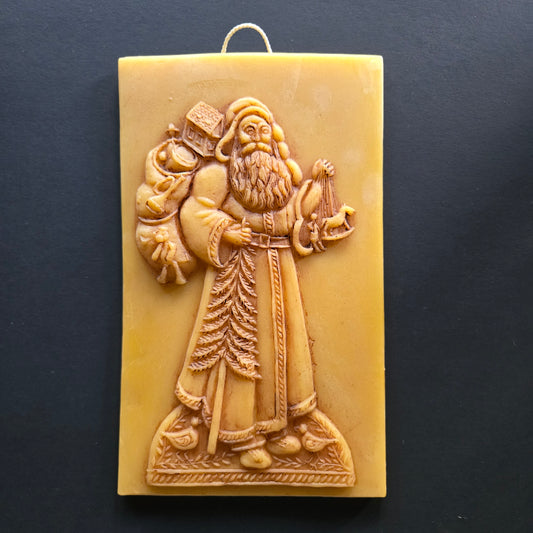 Decorative beeswax wall plaque with intricate design of Santa and toys on a dark background