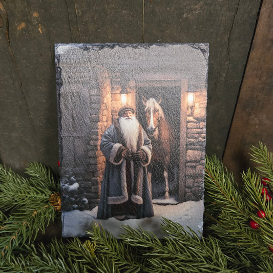Festive slate with a winter scene of a person and dog on a stone path, surrounded by Christmas greenery.