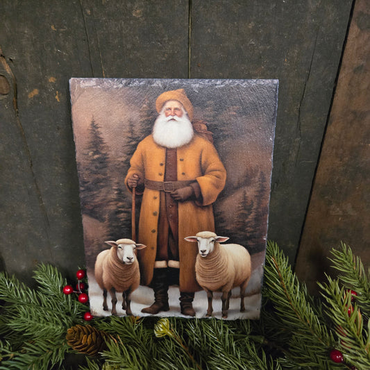 Framed picture of a man in a yellow coat with two sheep on a wooden surface with Christmas decorations.