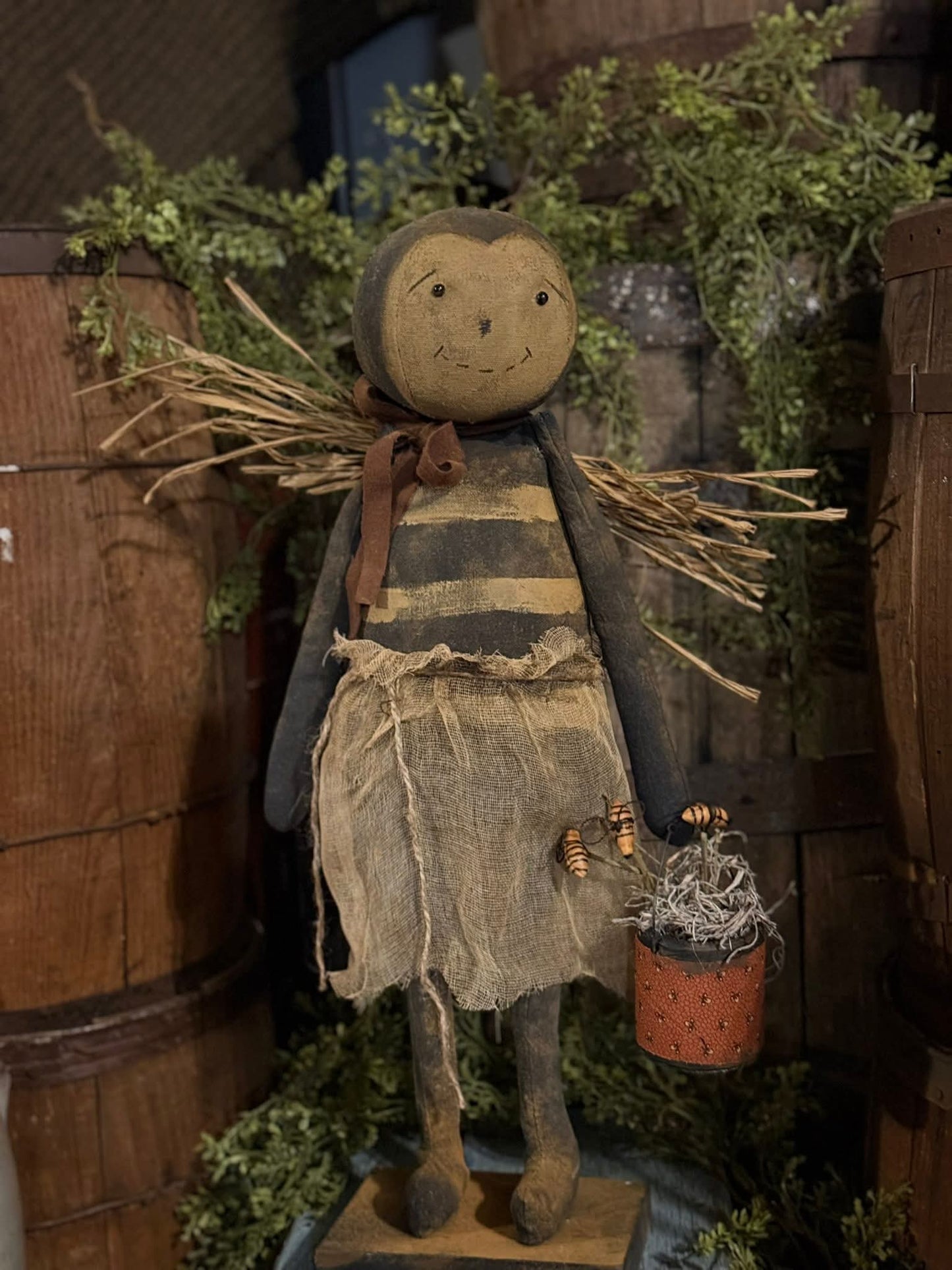 Textile doll with a rustic outfit and basket, standing against a wooden background.