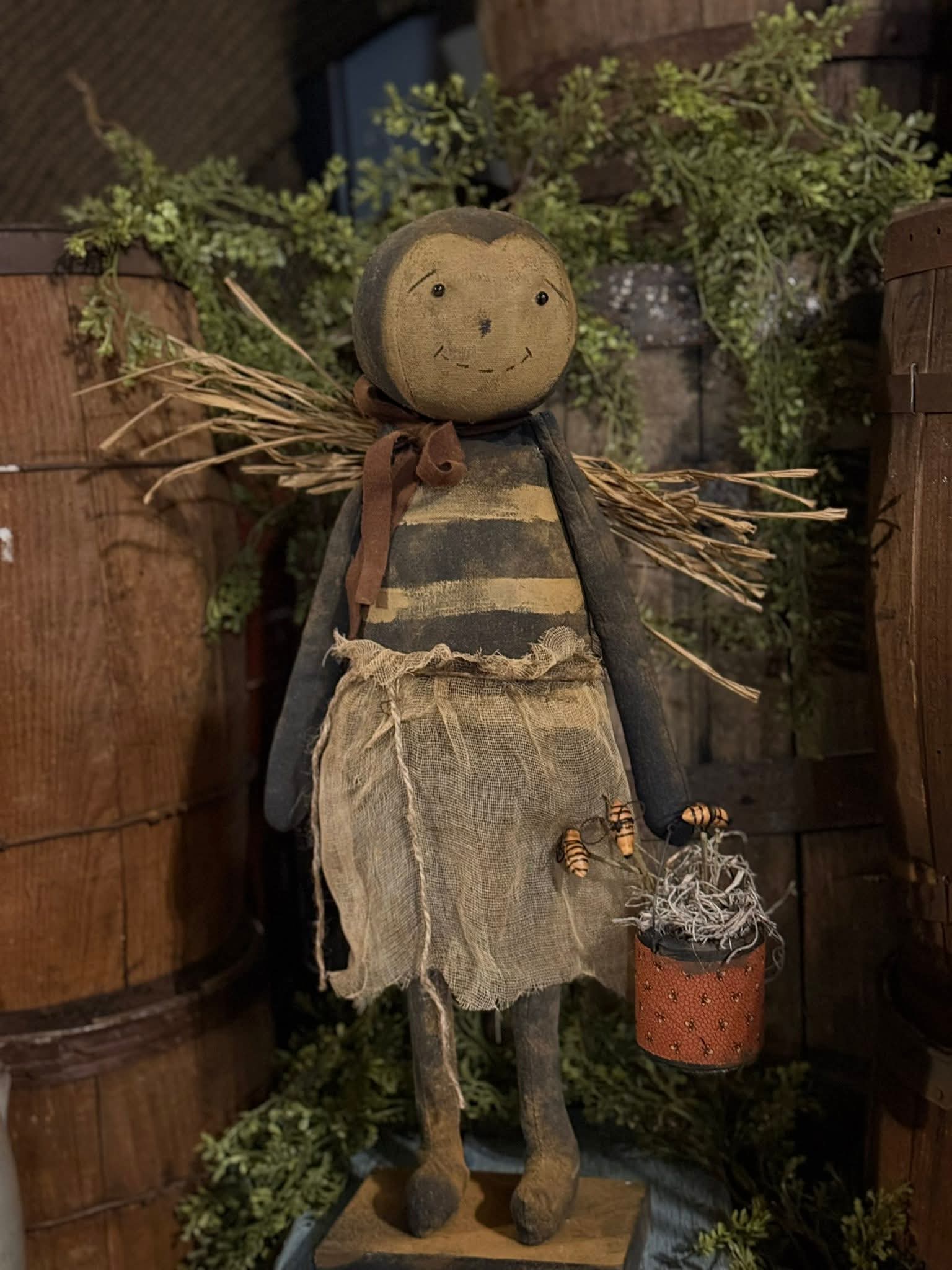 Textile doll with a rustic outfit and basket, standing against a wooden background.