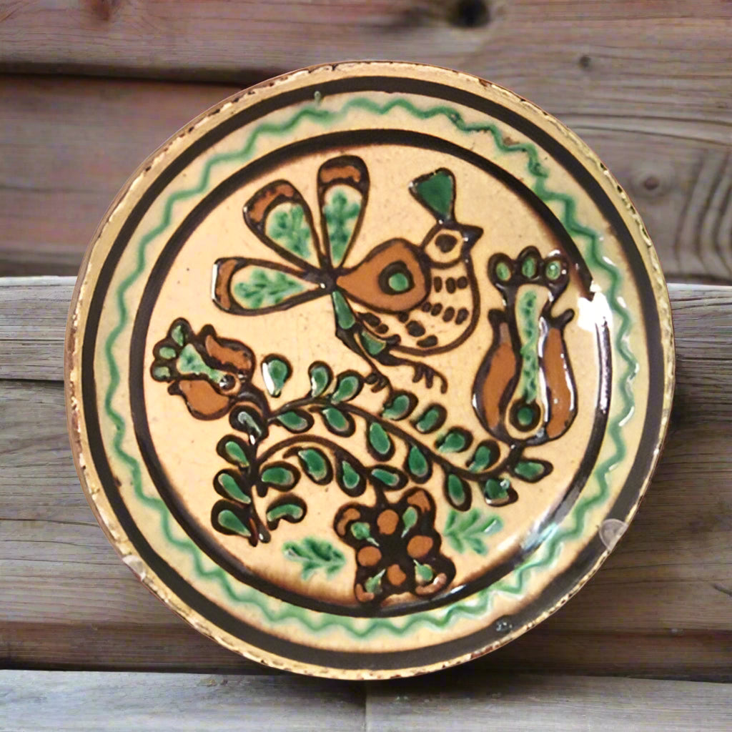 A ceramic plate with a bird and tulip design, featuring red, green, and brown colors against a beige background.