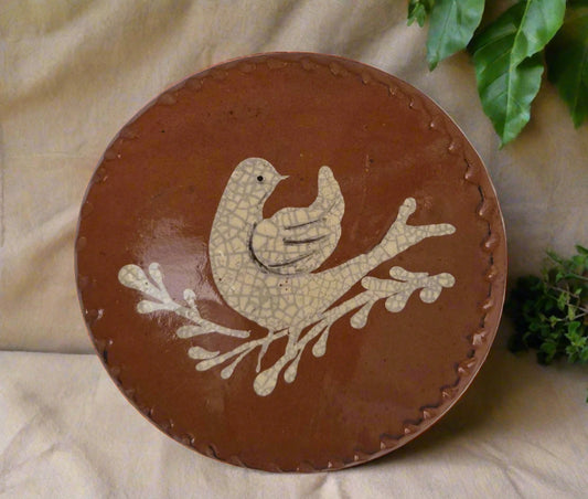 Small round redware plate with a cream color bird sitting on a vine